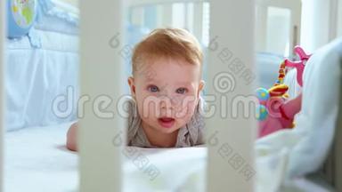 一个小孩在婴儿床上的特写镜头，笑着从婴儿床的格子间侧视。 快乐的童年，幼稚的快乐